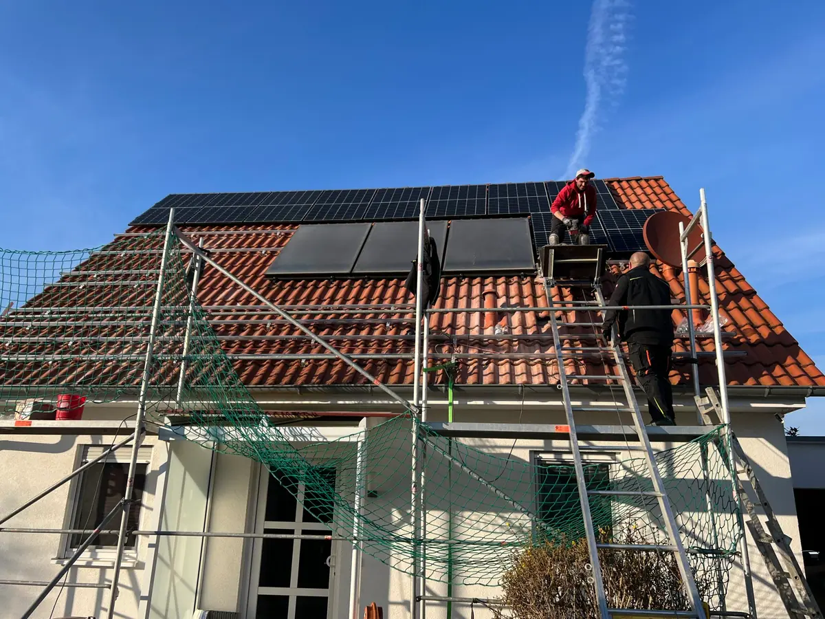 Zwei Monteure bauen auf einem eingerüsteten Einfamilienhaus eine Photovoltaikanlage auf